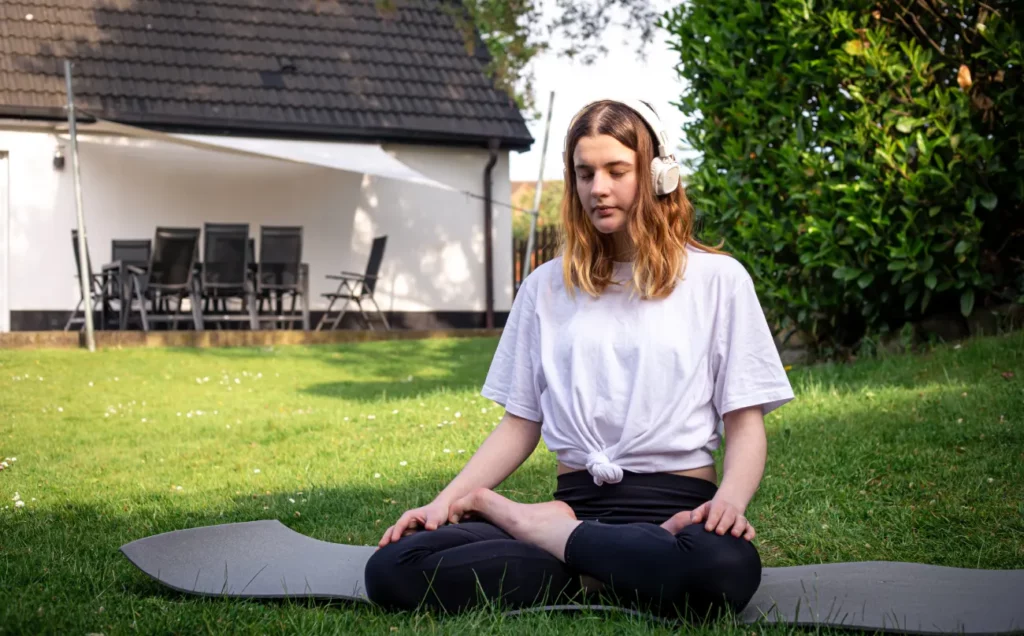 Ragazza seduta a gambe incrociate che medita in giardino per gestire meglio lo stress