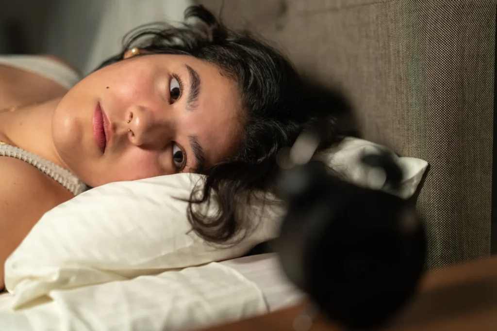 Ragazza a letto che guarda la sveglia di notte perché non riesce a dormire