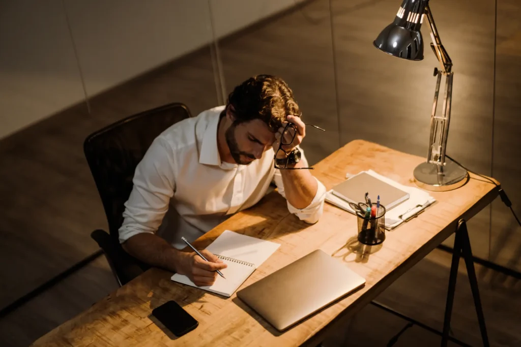 Uomo pensieroso che prende degli appunti seduto alla scrivania del suo ufficio